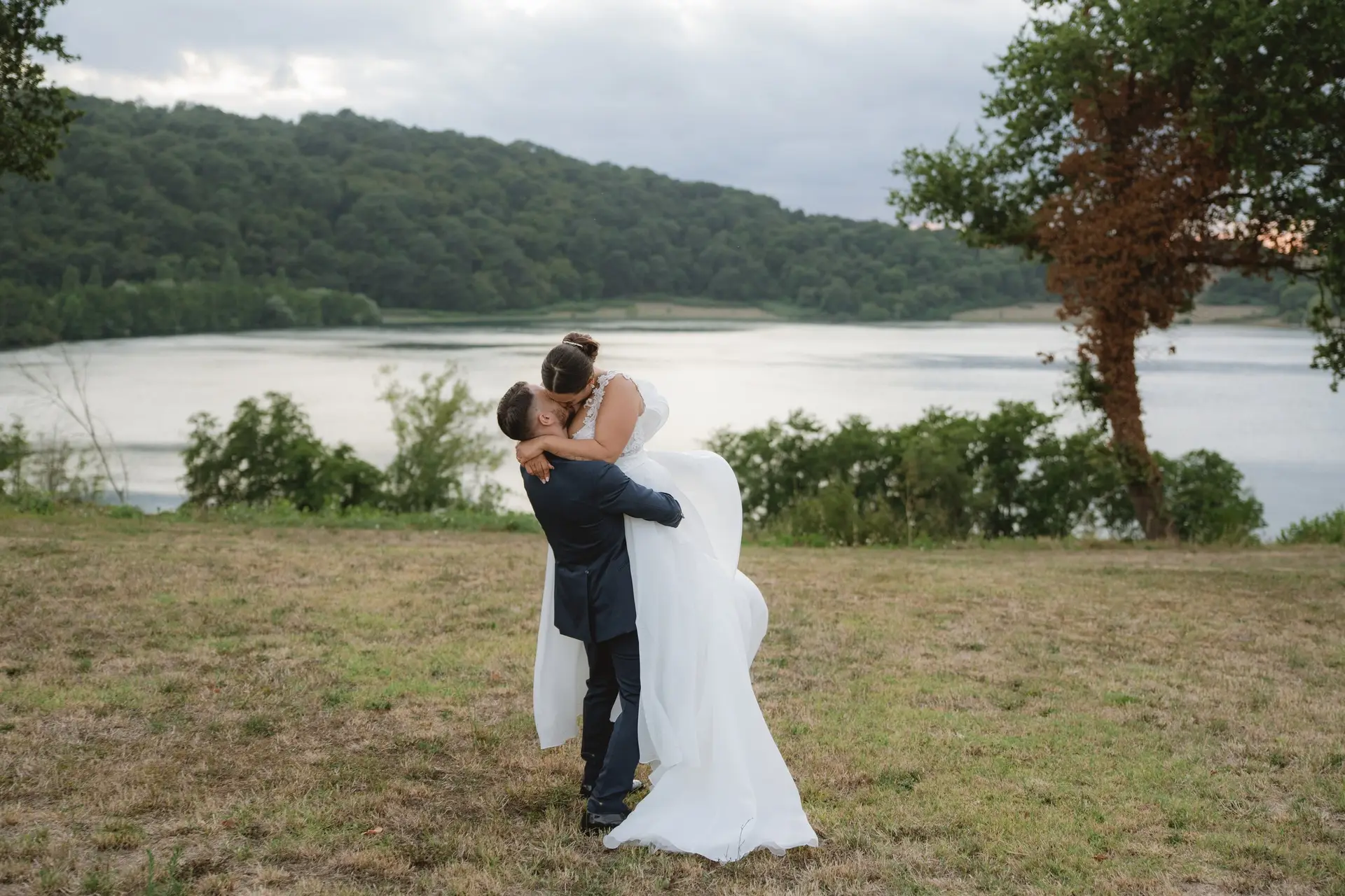The newlyweds embracing on the lawn with the lake behind them, at a real wedding at Frà Viaco