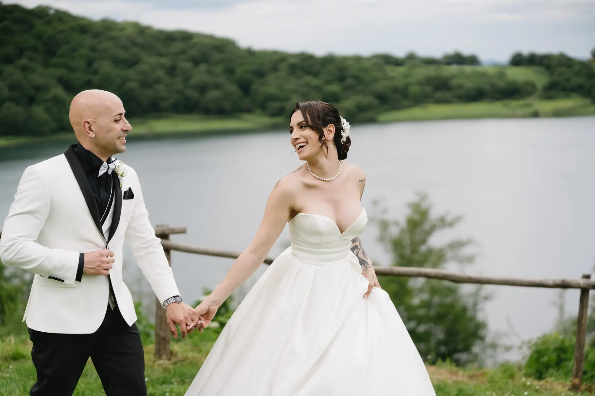 The couple hand in hand at the fence above Lago di Mezzano, at a real wedding at Frà Viaco