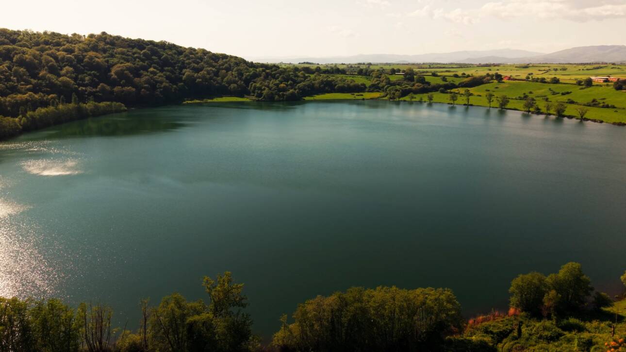Il Lago di Mezzano illuminato dal sole, circondato da boschi e campagna della Tuscia